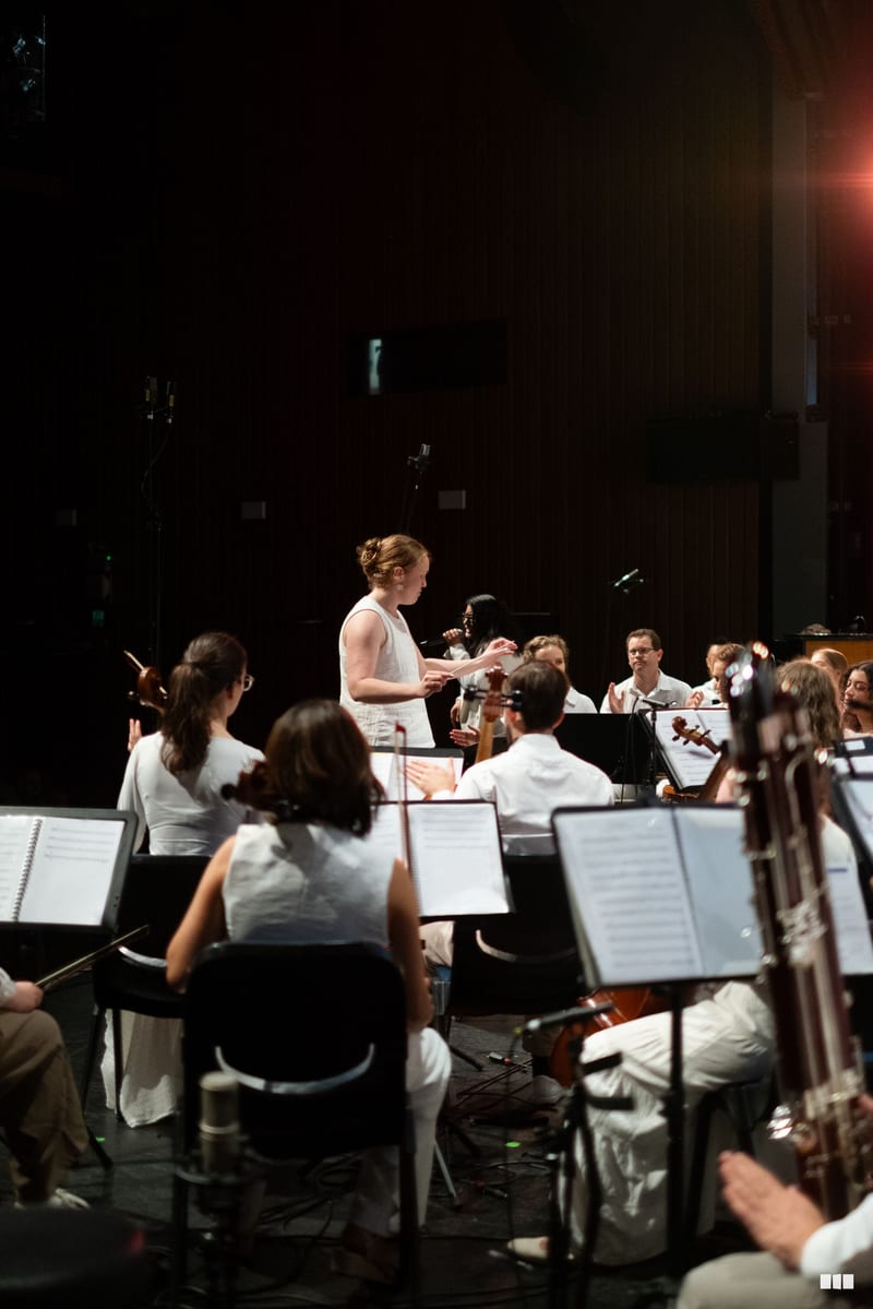 A conductor leads a string orchestra section during a rehearsal or performance on stage.