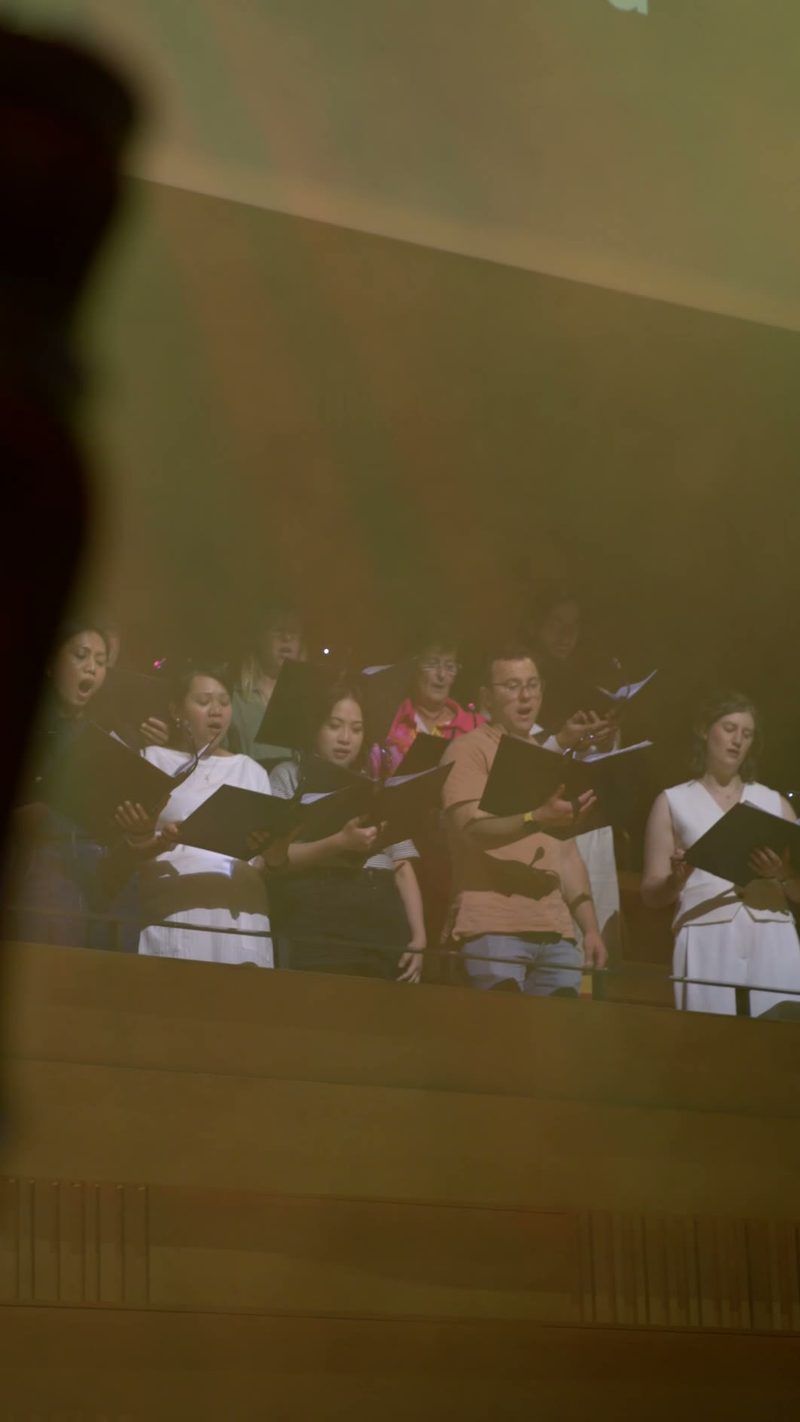A choir performs during a service, with singers holding hymnals and wearing formal robes with white stoles.