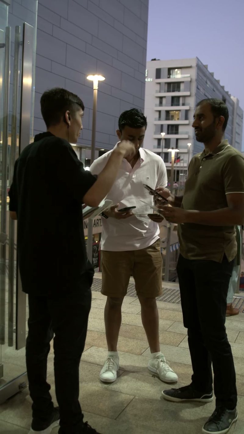 Three young men having a conversation outdoors in an urban plaza during evening hours.