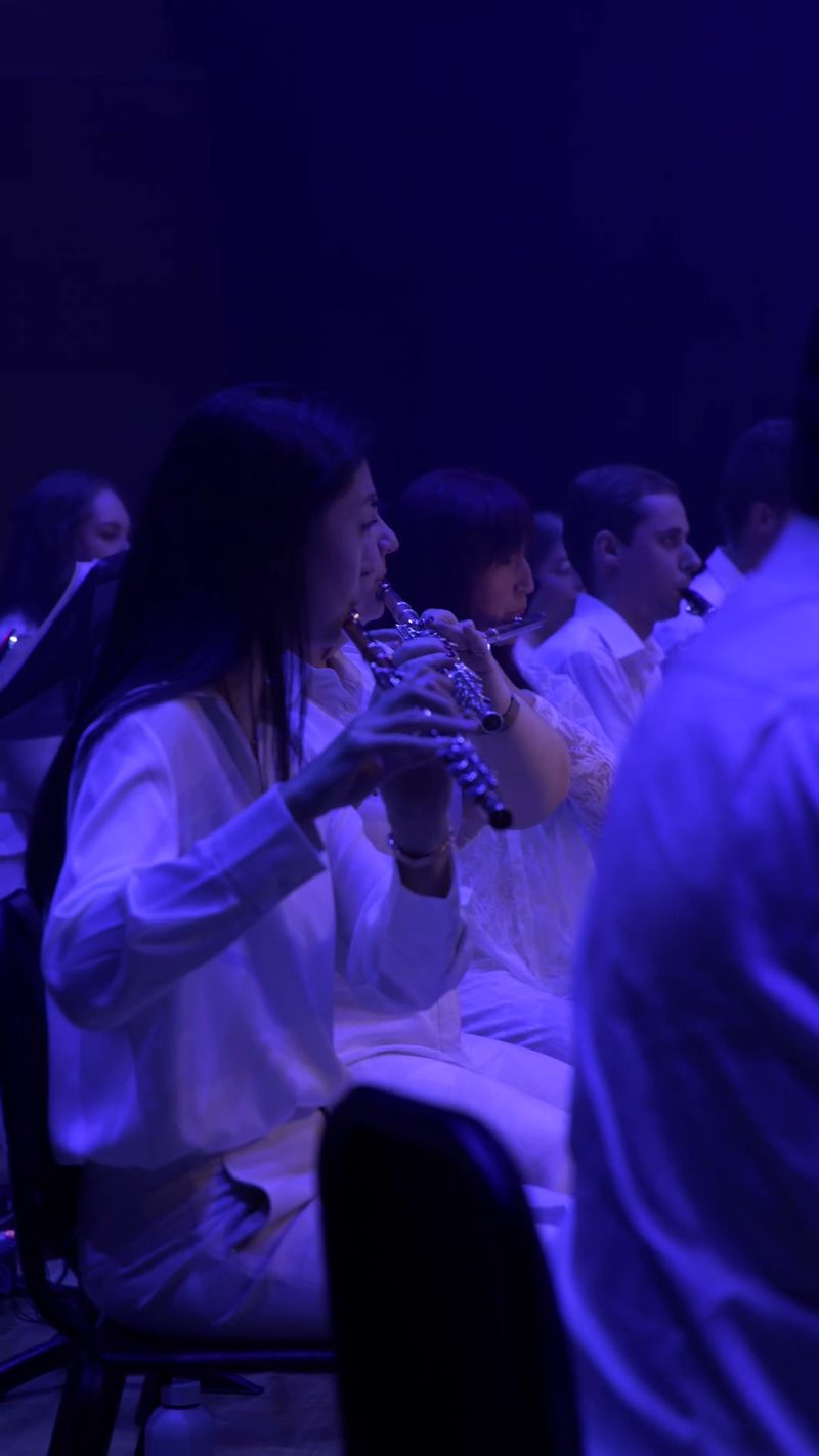 Choir members in white robes perform under blue stage lighting during a choral performance.