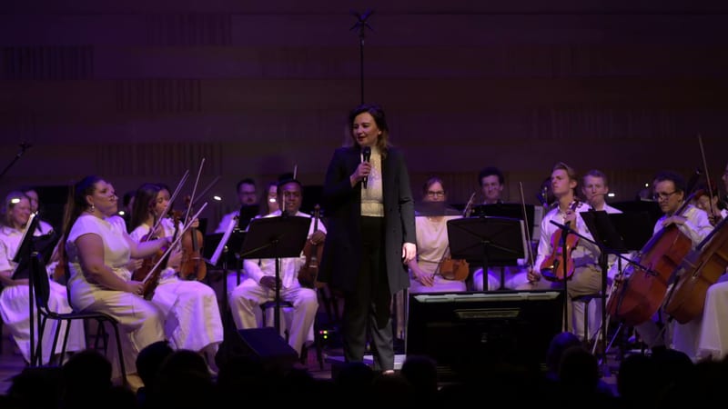 A conductor leads an orchestra of string players during a concert performance on stage.