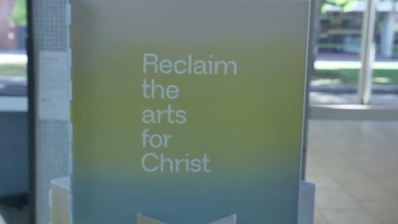 A frosted glass panel displays the text 'Reclaim the arts for Christ' in a modern institutional setting.