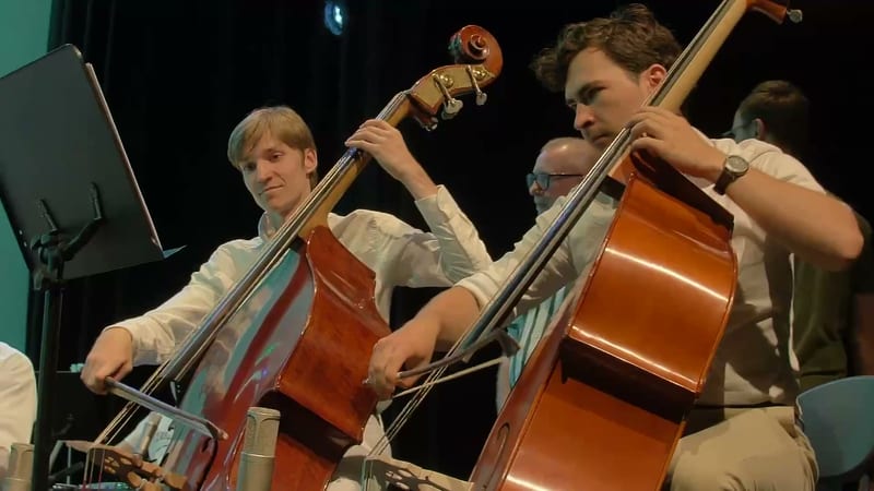 Two cellists perform together during an orchestral rehearsal or concert.
