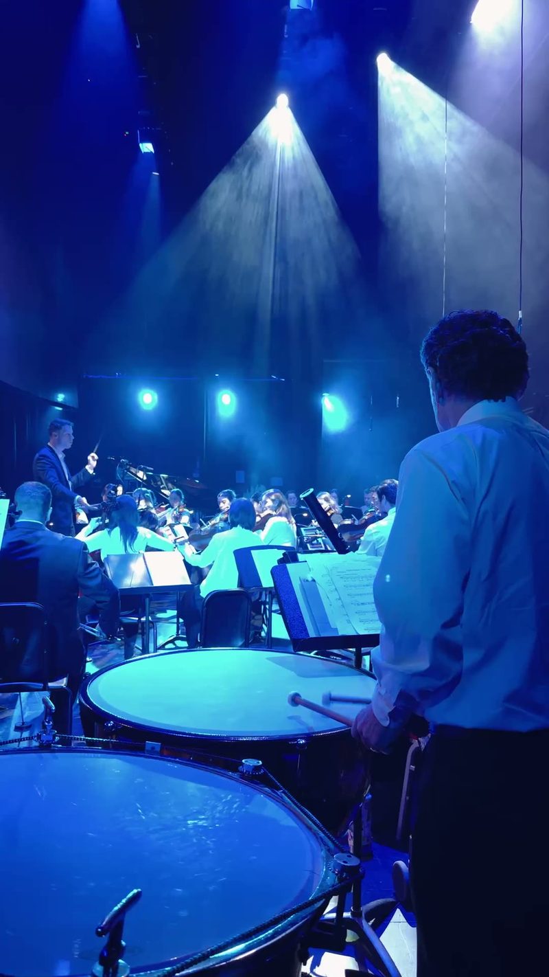 A conductor leads the orchestra during a performance with dramatic lighting.