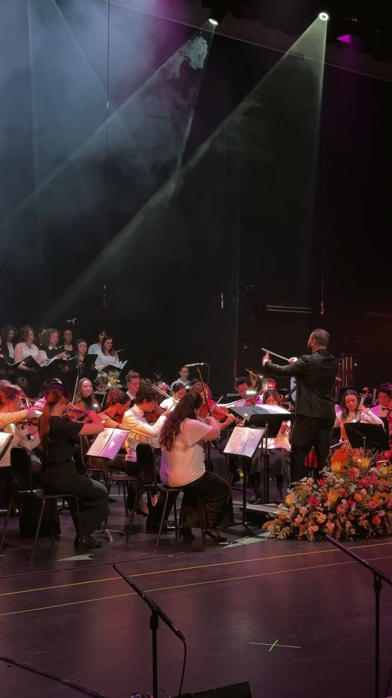 A symphony orchestra performs with a choir in a concert setting.