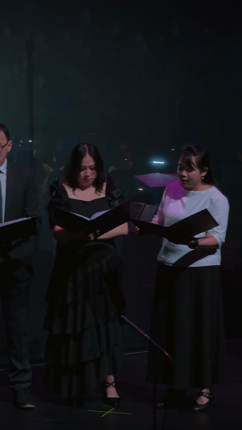 A group of singers performing on stage with music sheets.