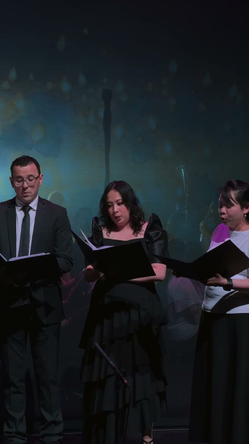 Three singers perform together on stage in front of a soft, colorful background.