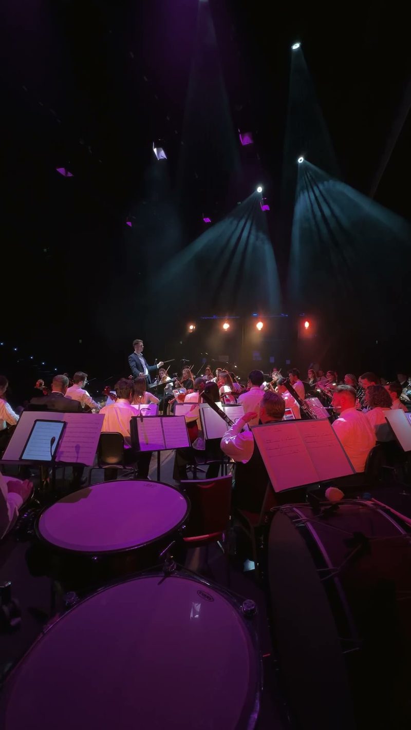 A view of a symphony orchestra performing on stage with dynamic lighting.