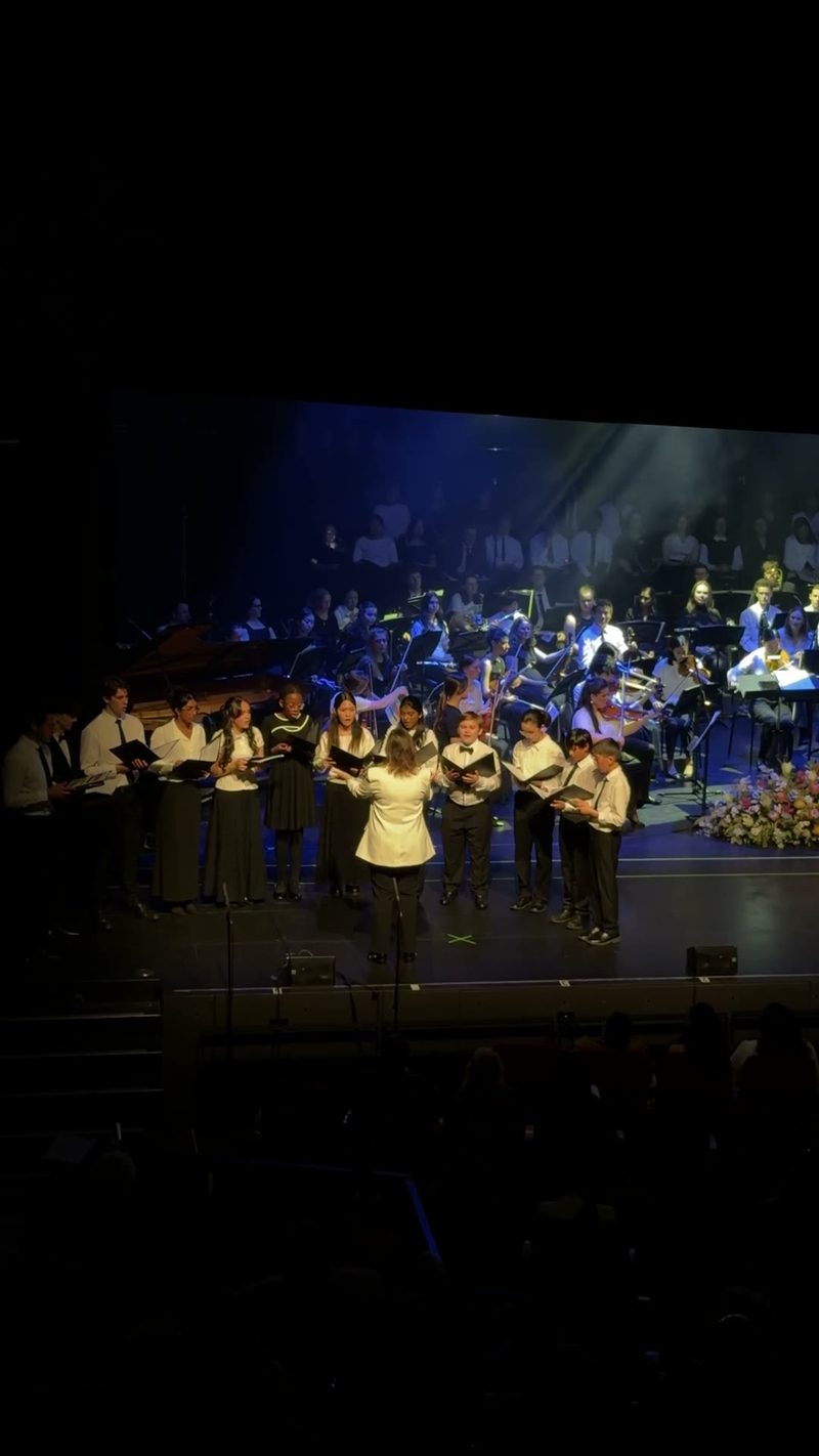 A choir performance during a symphony concert with musicians in the background.