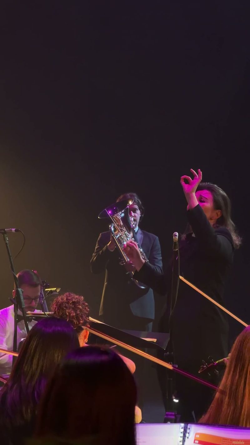 A musician playing a tuba while another conductor gestures during a performance.