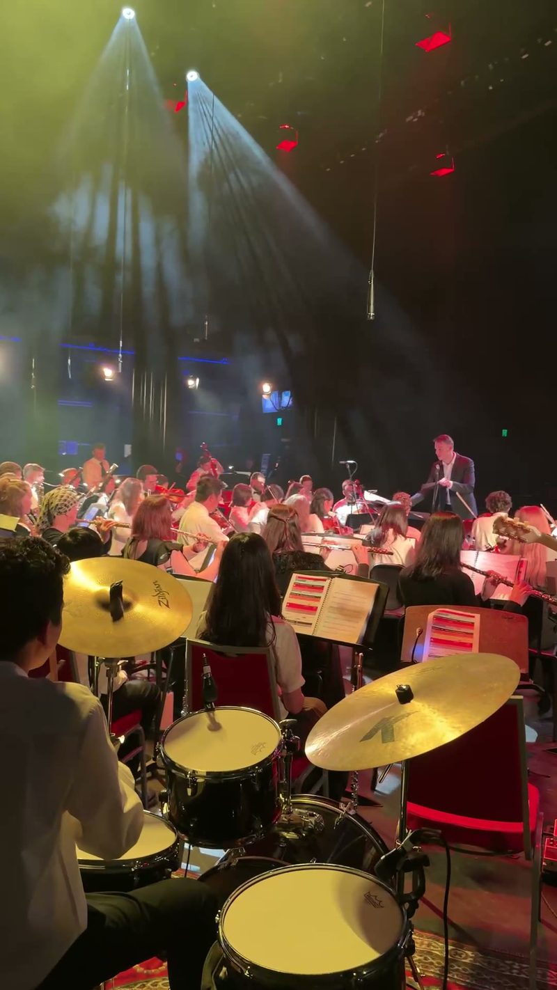 A full orchestra performing on stage under dramatic lighting.