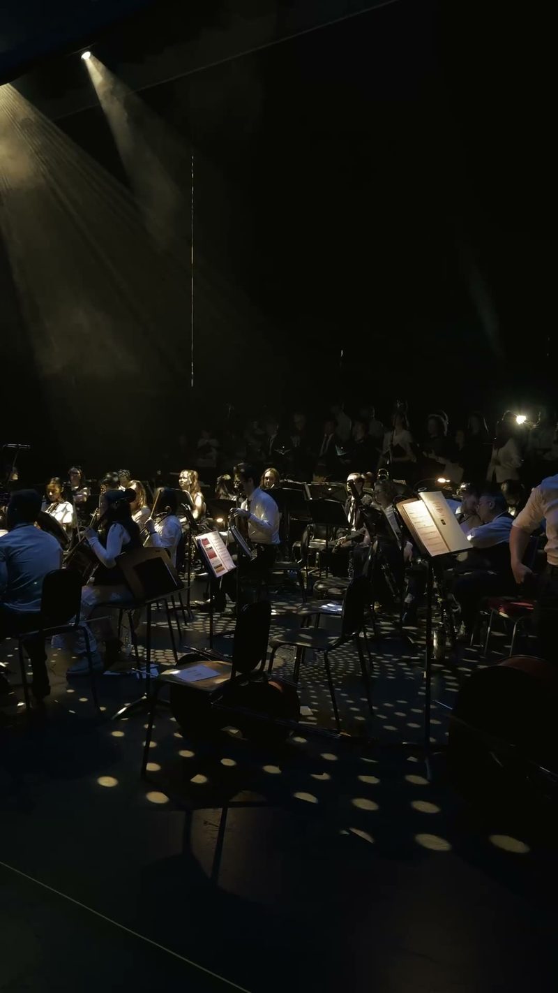 A symphony orchestra prepares to perform under dramatic lighting.