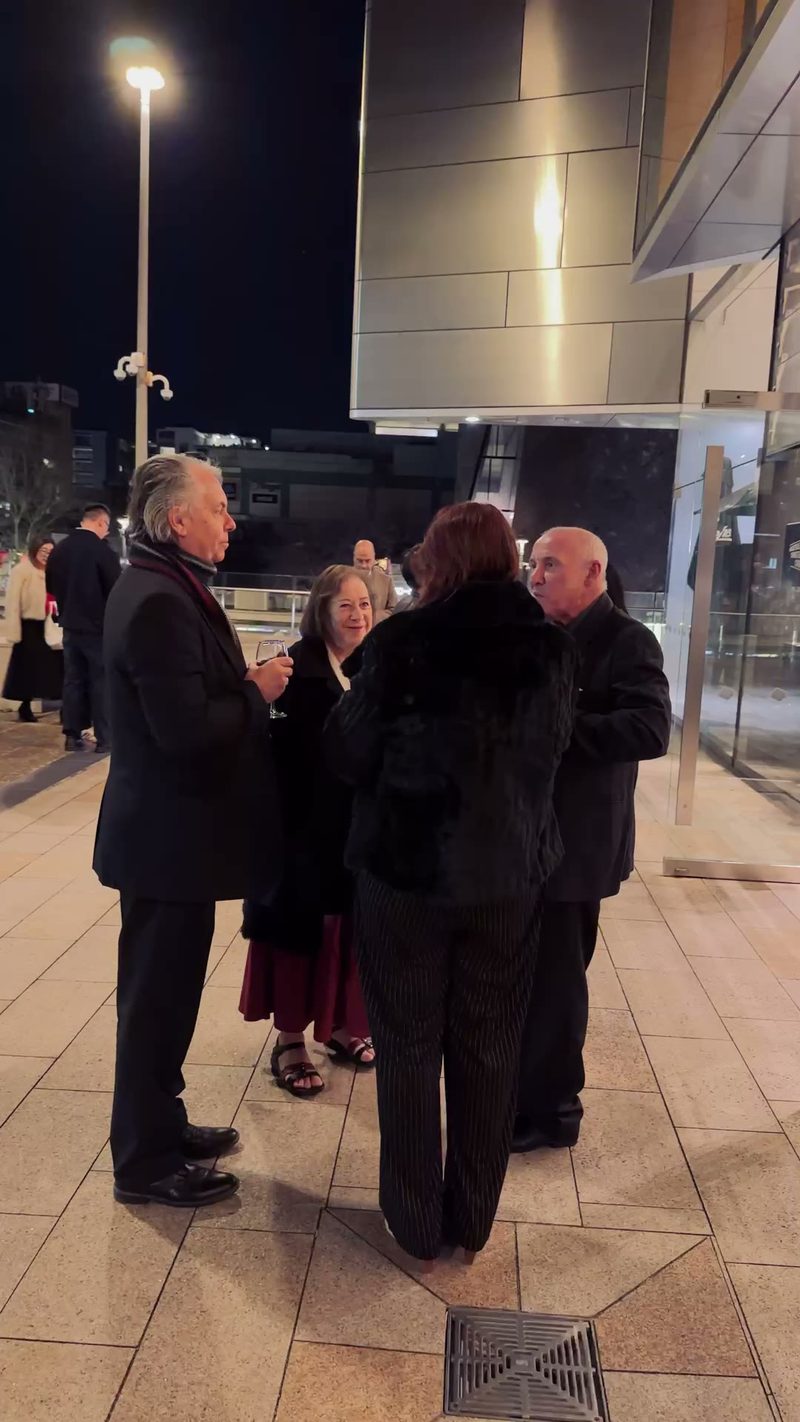 A group of people engaging in conversation outside an event venue at night.