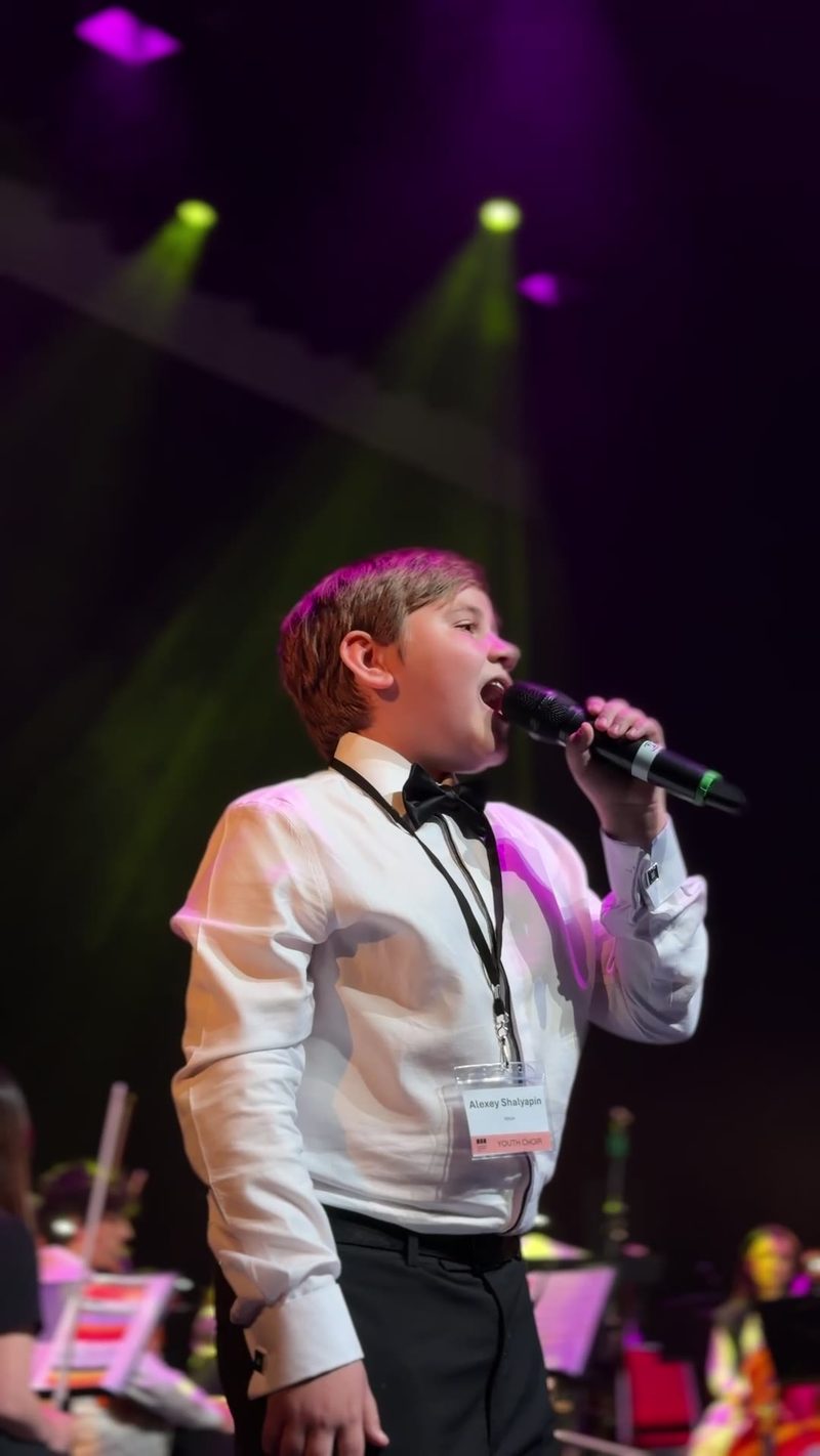A young boy passionately singing into a microphone on stage during a performance.