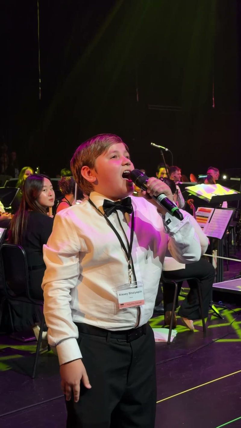 A young soloist performs on stage in front of a choir and orchestra.