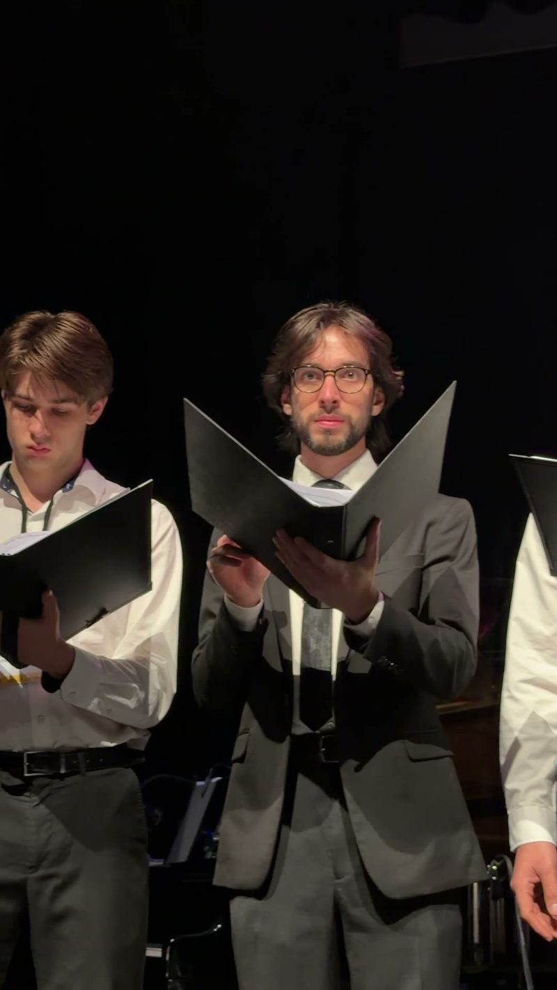 Three male choir members reading from their sheet music during a performance.